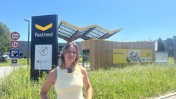 Frau steht vor einer großen Ladestation mit Solardächern und einem Kiosk