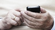 Das Bild zeigt eine ältere Person, die ein Smartphone in der Hand hält.