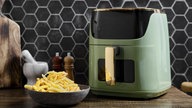 Symbolbild Airfryer: Eine Luftfritteuse befindet sich auf einer Holzarbeitsplatte in einer Küche. 