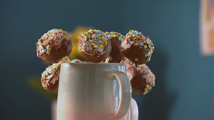 Es sind mehrere Cake Pops mit Schokolade und Streußel am Stiel in einer Tasse