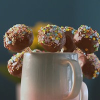 Es sind mehrere Cake Pops mit Schokolade und Streußel am Stiel in einer Tasse