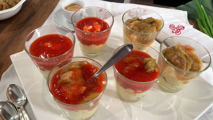 Grießpudding in sechs Glasschalen angerichtet, jeweils mit Rhabarber- oder Erdbeersoße
