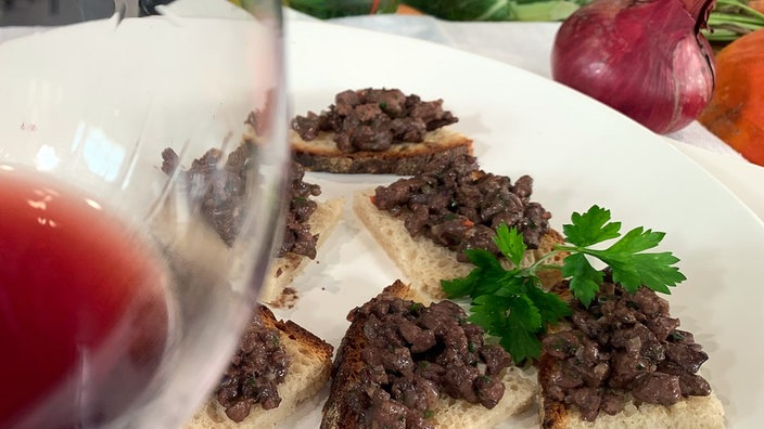 Hühnerleberhäckerle auf Brotscheiben angerichtet zu einem Glas Rotwein