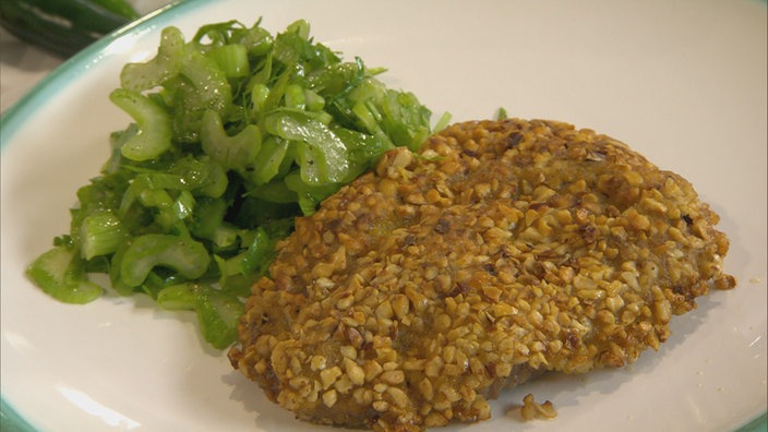 Lammschnitzel mit Haselnussknusper und Selleriesalat auf einem Teller angerichtet