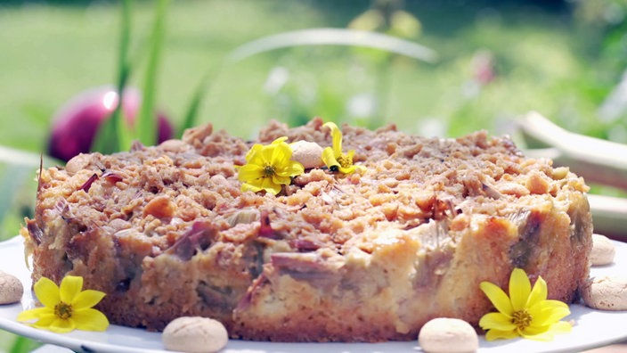 Rhabarberkuchen auf einer Drehplatte mit paar echten gelben Blumen und Amarettinikeksen verziert.