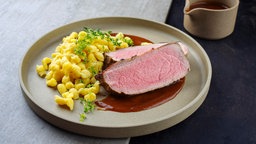 Auf einem Teller ist Rinderbraten mit Spätzle und einer feinen braunen Soße angerichtet.