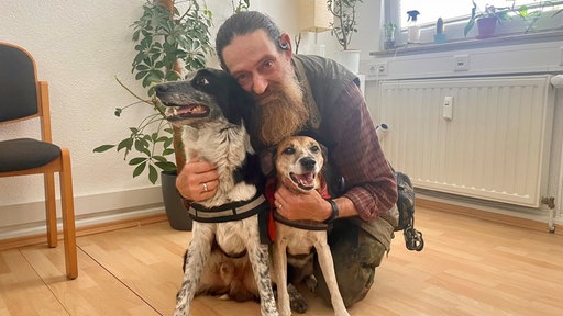 Ein älterer Mann mit seinen zwei Hunden im Bild.