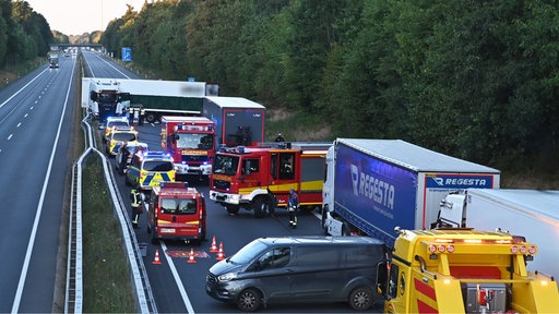 Ein LKW steht nach einem Unfall quer auf einer Autobahn und mehrere Einsatzfahrzeuge von Feuerwehr und Polizei stehen vor der Unfallstelle.