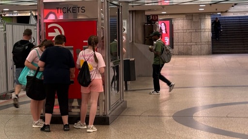 Eine Frau steht mit zwei Kindern an einem Ticketautomat.