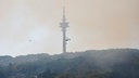 Helikopter mit Löschwasser-Außenlastbehälter beim Waldbrand im Hürtgenwald vor einem Turm