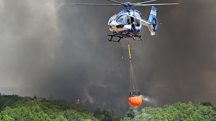 Helikopter der Polizei mit Wasser in einem Löschwasser-Außenlastbehälter beim Waldbrand im Hürtgenwald