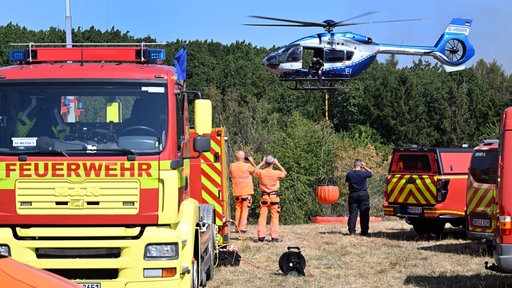 Ein Helikopter der Bundespolizei nimmt Wasser neben Feuerwehrfahrzeugen auf beim Brand im Hürtgenwald
