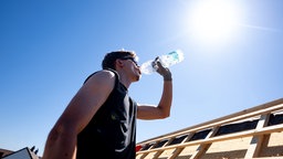 Ein junger Mann trinkt draußen in der Sonne Wasser aus einer Flasche