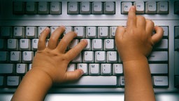 Die Hände eines Kleinkindes auf der Tastatur eines Computers