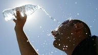 Junger Mann schüttet sich eine Wasserflasche über den Kopf