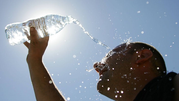 Junger Mann schüttet sich eine Wasserflasche über den Kopf