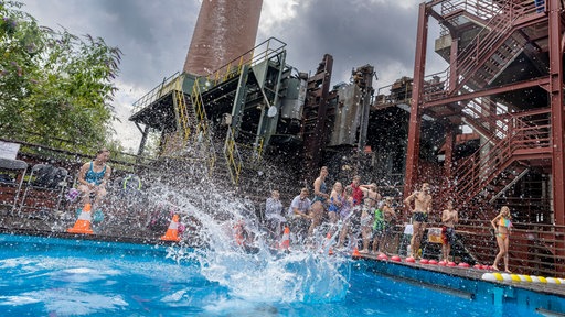 Ein Teilnehmer erzeugt mit seiner Arschbombe eine riesige Wasserfontäne vor der Kulisse der Zeche Zollverein