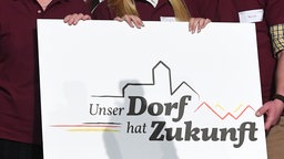 Personen halten ein Schild mit der Aufschrift «Unser Dorf hat Zukunft» in den Händen