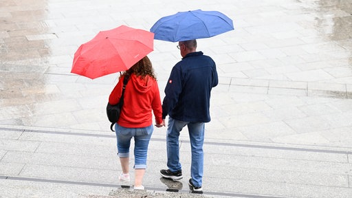 Zwei Personen mit Regenschrimen laufen eine Treppe hinab