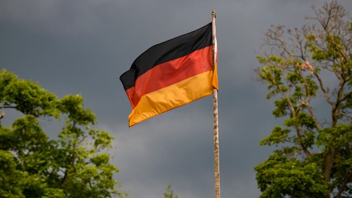 Die deutsche Flagge weht in Schwarz-Rot-Gold vor dunklen Wolken im Wind