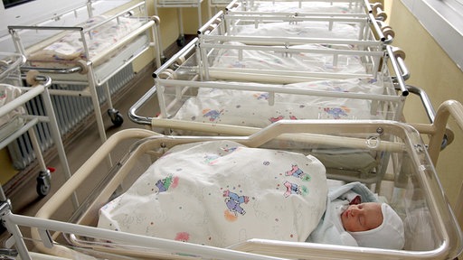 Ein Baby liegt in einem Bett auf der Neugeborenstation, die anderen Betten sind leer.