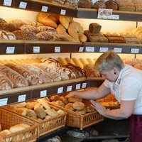 Eine Verkäuferin steht in einer Bäckerei vor einem Regal mit Brötchen und Broten.