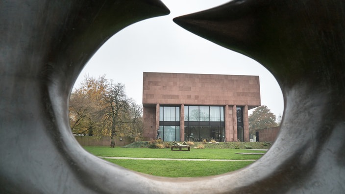 Blick durch eine Loch einer schwarzen Skulptur auf das rötliche Gebäude der Kunsthalle in Bielefeld