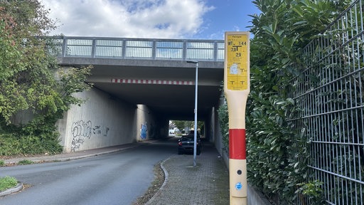 Gelbes Schild steht am rechten Rand einer Straßenunterführung