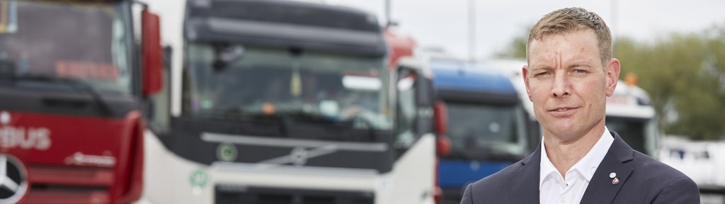 BGL Vorstandssprecher Dirk Engelhardt steht mit verschränkten Armen auf einem Parkplatz. Im Hintergrund sind unscharf LKW zu sehen.