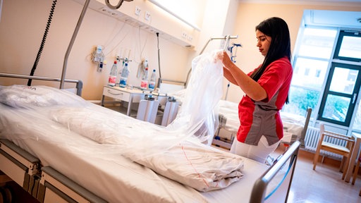 Eine Frau zieht die Folie von einem neuen Krankenhausbett ab.