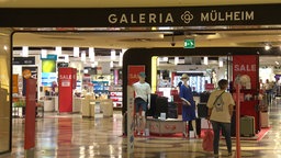 Der Eingang von Galeria in Mülheim, gefilmt von außen, Kunden betreten das Geschäft