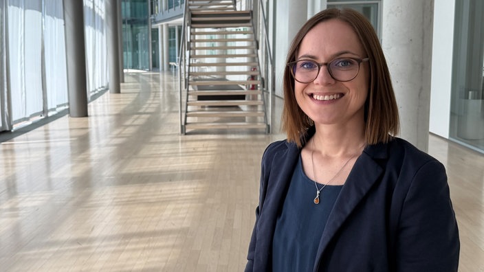 Julia Römhild steht in einem Gebäude mit langem Flur in der Universität.