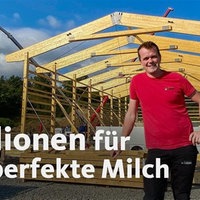 Ein Mann in einem roten Shirt steht vor einer noch nicht fertig gebauten Halle