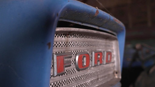 Auf der Front eines alten blauen Traktors steht in roten Buchstaben die Marke "Ford".