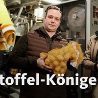 v. l. Reinhard Krebbers und Sohn Niklas. Sie stehen vor einer Maschine und halten Kartoffelsäcke in den Händen.