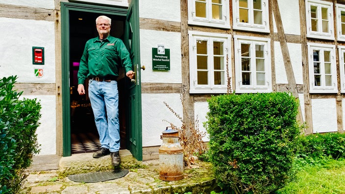 Friedrich Wilhelm Haver-Rassfeld steht draußen auf einer Treppenstufe zwischen einer geöffneten Gebäudetür und drückt die Türklinke herunter.