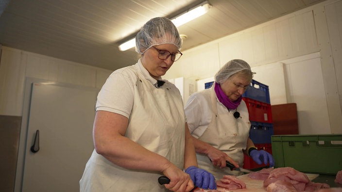 Anne Korte und ihre Mutter Hedda stehen mit Haarnetzen bekleidet in der Schlachterei des Geflügelhofs und schneiden Fleisch