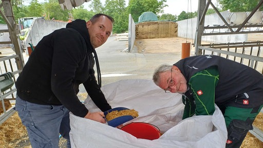 Philipp Terhorst und Erwin Köster holen auf dem Milchhof Getreide aus einem großen weißen Sack