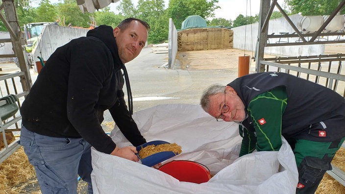 Philipp Terhorst und Erwin Köster holen auf dem Milchhof Getreide aus einem großen weißen Sack