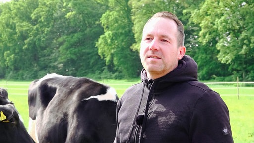 Philipp Terhorst steht auf der Weide eines Milchhofes im Münsterland, hinter ihm eine schwarz-weiß gefleckte Kuh