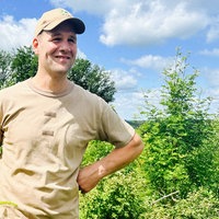 Der Landwirt und Waldbesitzer Torsten Dörmbach steht auf seinem Waldgrunstück. Er ist umgeben von Bäumen und Pflanzen und lächelt zufrieden.