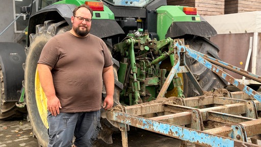 Landwirt Julian Freisendorf steht vor einem seiner Traktoren und schaut in die Kamera.