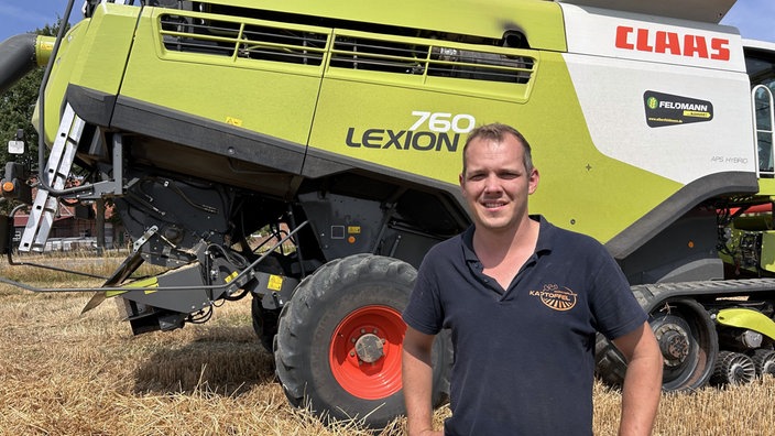 Landwirt Fabian Schulze Messing auf dem Getreidefeld vor einem Mähdrescher