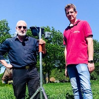 Zwei Männer stehen mit einem Bewegungsmelder auf einem grünen Feld.