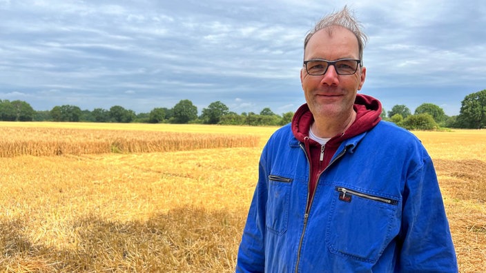 Landwirt Thomas Döring steht vor einem gelben Weizenfeld und schaut lächelnd in die Kamera