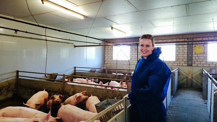 Sandra Löbert in blauem Schutzanzug, links neben ihr Schweine in Ställen.