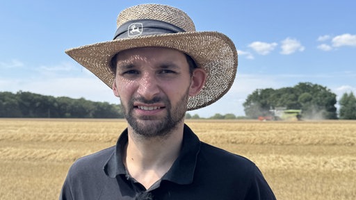 Jan Große Kleimann auf seinem Feld, im Hintergrund ein Mähdrescher bei der Ernte.