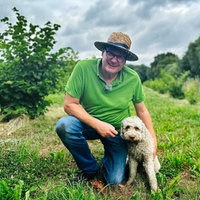 Burkhard Kleffmann, grünes Polo-Shirt, Strohhut, Brille, blaue Jeans, hockt im Gras rechts neben ihm sitzt seine Hündin Betty.
