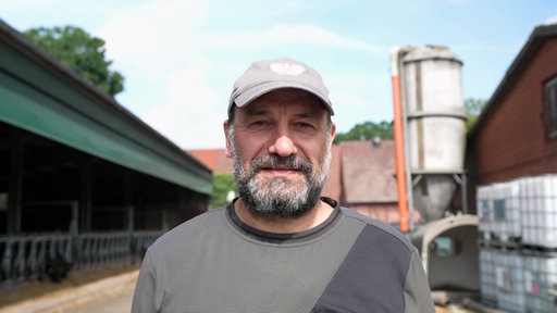 Der Bauer Reinhard Höltmann guckt in die Kamera und im Hintergrund zeigt sich sein Hof.