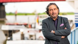 Roberto Spranzi steht mit verschränkten Armen vor einem Hafen